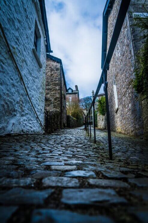 Cobblestone footpath with handrail in the centre. Old style houses line the footpath.