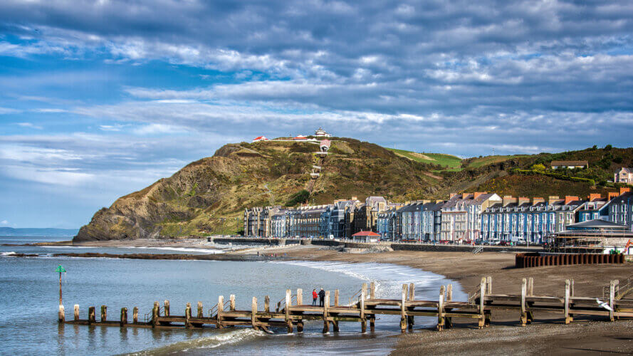 A view of Aberystwyth's coastal seafront with a cliff-top in the background.