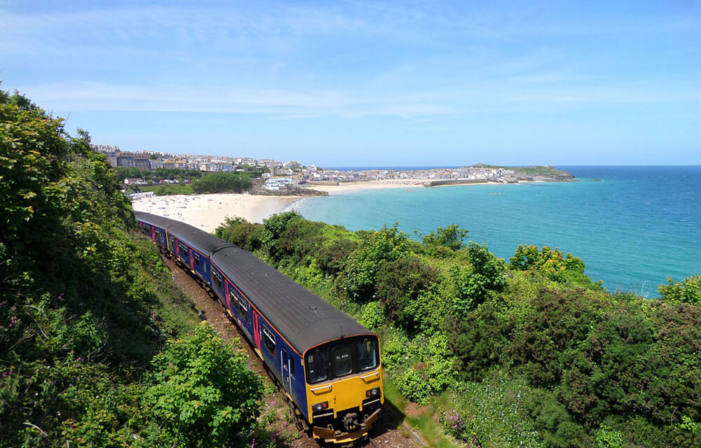 A Great Western Railway train traversing the line between St Erth and St Ives, with a view of the bay in the background.